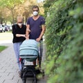 Worried young parent walking on empty street with stroller wearing medical masks to protect them from corona virus