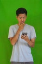 Worried young South Asian male looking down at his phone on green background Royalty Free Stock Photo