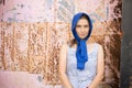worried young woman with blue headscarf standing in front metal background with splattered paint