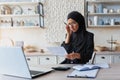 Worried young woman in hijab checking her accounts, budget, expenses at home. Sitting at home in the kitchen with a Royalty Free Stock Photo