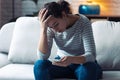 Worried young woman using her mobile phone while sitting on sofa in the living room at home Royalty Free Stock Photo