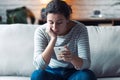 Worried young woman using her mobile phone while sitting on sofa in the living room at home Royalty Free Stock Photo