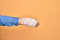 Wounded hand of caucasian young woman cover with bandage doing handshake gesture over isolated yellow background