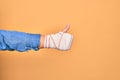 Wounded hand of caucasian young woman cover with bandage doing ok sign with thumb up over isolated yellow background