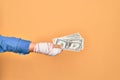 Wounded hand of caucasian young woman cover with bandage holding bunch of dollars banknotes over isolated yellow background