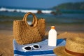 Woven bag, white sunglasses rest on blue striped towel. Bottle of sunscreen, straw hat nearby. Sandy beach setting with Royalty Free Stock Photo