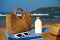 Woven tote bag stands beside sunscreen bottle on striped blue towel at sunny tropical beach. Sun hat and white Royalty Free Stock Photo
