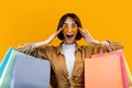 Wow, big sale. Emotional young woman wearing and touching sunglasses holding colorful shopping bags, yellow background Royalty Free Stock Photo