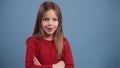 Wow expession. Little caucasian girl in red sweater showing thumbs up and positively smiling, isolated on blue