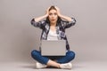 Wow, great news! Happy young amazed woman sitting on the floor with crossed legs and using laptop isolated on gray background Royalty Free Stock Photo