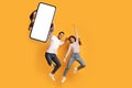 Wow, great news. Overjoyed couple showing huge smartphone with blank white screen, jumping and celebrating victory Royalty Free Stock Photo