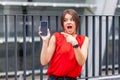 Wow, incredible mobile service! Portrait of shocked attractive young woman pointing at smartphone. outdoor