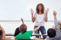 Wow, one at a time guys. A young teacher standing at the front of her classroom full of students with raised hands. Royalty Free Stock Photo