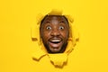 Wow. Overjoyed black man with open mouth breaking and looking through hole in slit yellow paper, copy space Royalty Free Stock Photo
