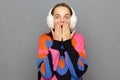 Wow. Photo of young woman wearing white fluffy ear warmers and colorful sweater, feeling shocked and deeply surprised, posing Royalty Free Stock Photo