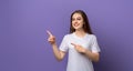 Portrait of young woman pointing fingers aside and looking with positive face expression, standing over purple background Royalty Free Stock Photo