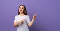 Portrait of young woman pointing fingers aside and looking with positive face expression, standing over purple background Royalty Free Stock Photo