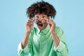 Wow. Shocked black guy touching his glasses and opening mouth, looking at camera on blue background Royalty Free Stock Photo