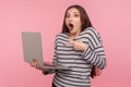 Wow, unbelievable! Portrait of shocked young woman in striped sweatshirt standing with open mouth and pointing at laptop