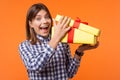 Wow, what a present! Portrait of young brunette woman with charming smile holding gift. isolated on orange background