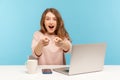 Wow, you`re awesome! Amazed excited woman employee sitting at desk with laptop and pointing to camera