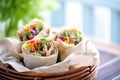 wrapped pulled pork burritos in a basket with napkins