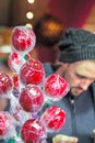 Wrapped toffee apples on display with an unrecognised male customer in the background at Christmas market