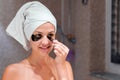 Wrapped in towel after bath woman is looking in the mirror and taking off eye patches. She is pleased with the effect. Remove dark