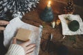 Wrapping christmas gift. Hands wrapping simple gift box in festive blue paper on rustic wooden table background with candle,