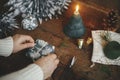 Wrapping christmas gift. Hands wrapping simple gift box in festive blue paper on rustic wooden table background with candle,