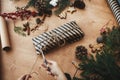 Wrapping rustic christmas present. Hands wrapping christmas gift in stylish striped paper and pine branches, cones, gingerbread