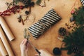 Wrapping rustic christmas present. Hands wrapping christmas gift in stylish striped paper and pine branches, cones, gingerbread