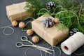 Wrapping rustic eco Christmas gifts with craft paper, string and natural fir branches on dark background