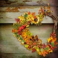A wreath of autumn leaves and berries in heart shape on wooden background