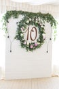 Wreath of eucalyptus leaves and peonies on a wooden white wall with the number ten inside