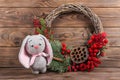 Wreath and hare rabbit. Christmas winter frame on dark wooden background. Red elements Crochet Kraft Toys