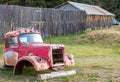 Wreck of an ancient rusty car in front of the wooden fence and barn