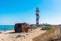 Wreckage of nautical buoy and boat on beach with tourist around lighthouse