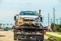 Wrecked car with mud and plant material sticking out of grill and from under hood on flatbed truck in city - possible in flood -