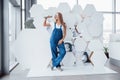 Wrench in hand. Girl in blue uniform stands against abstract wall with white pieces of surface in the shape of hexagon