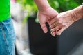 Wrinkled elderly woman`s hand holding to young man`s hand, walking in shopping mall park. Family Relation, Health, Help, Support, Royalty Free Stock Photo