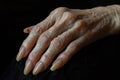 Wrinkled hand of elderly woman with long fingernails resting on a black background Royalty Free Stock Photo