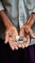 Wrinkled hands clutching coins illustrate senior man as he saves money with limited pension