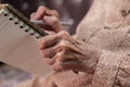 wrinkled hands for elderly person writing notes on here note book in living room Royalty Free Stock Photo