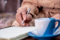 wrinkled hands for elderly person writing notes on his note book while drinking coffee Royalty Free Stock Photo