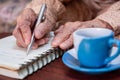 wrinkled hands for elderly person writing notes on his note book while drinking coffee Royalty Free Stock Photo