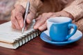 wrinkled hands for elderly person writing notes on his note book while drinking coffee Royalty Free Stock Photo