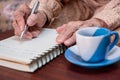 wrinkled hands for elderly person writing notes on his note book while drinking coffee Royalty Free Stock Photo