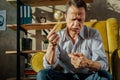 Wrinkled old man sitting on a yellow armchair and taking pills