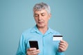 Wrinkled successful mature businessman in formal clothes holds modern cell phone and plastic card, checks his bank account or make Royalty Free Stock Photo